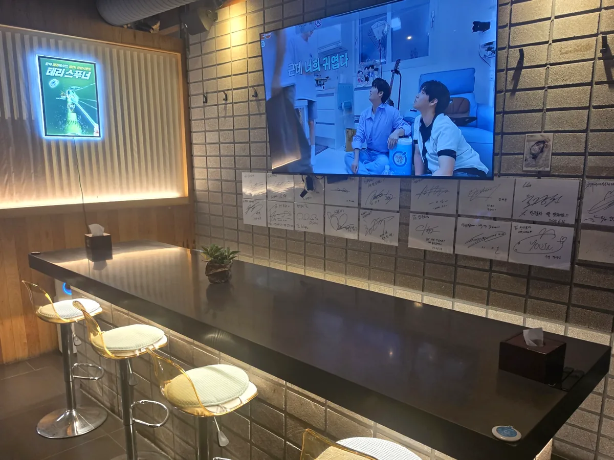 TV가 켜진 친구포차 바 좌석 — 타일 벽에 손님들이 남긴 메모